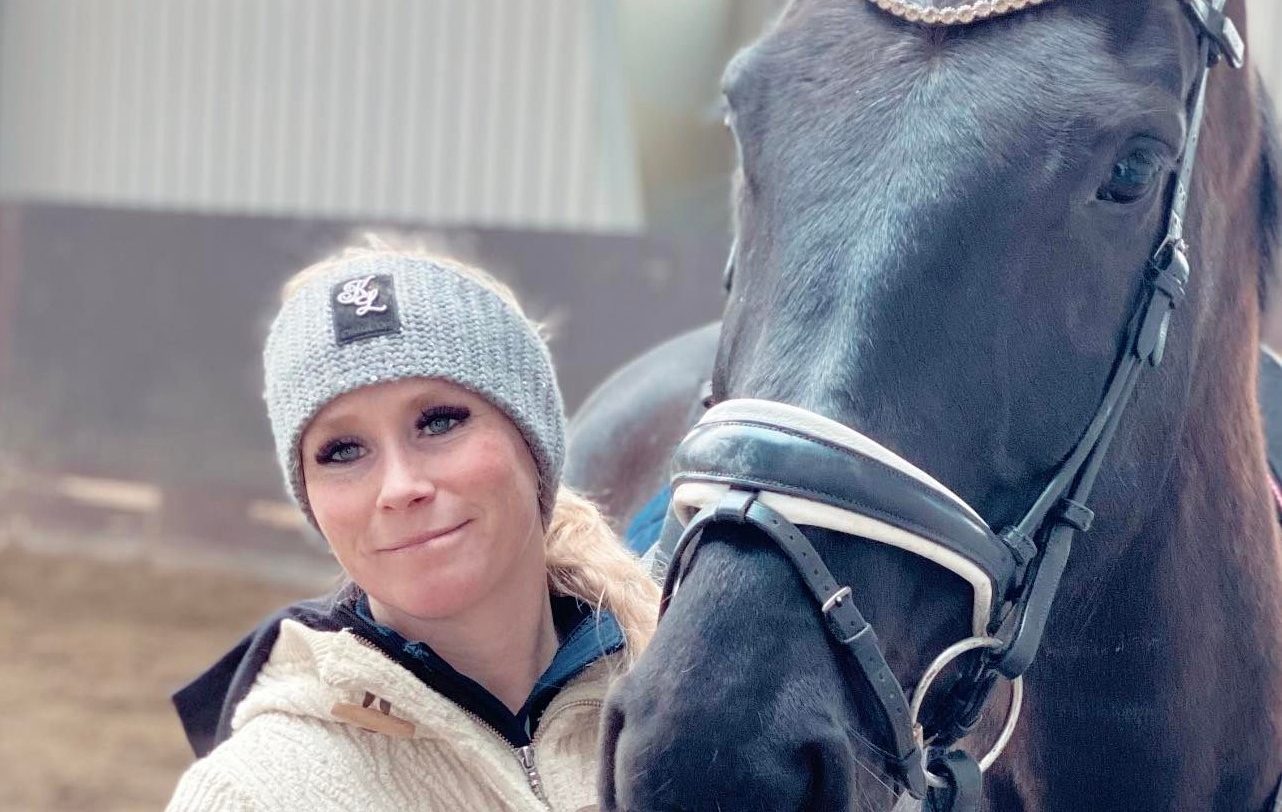 Hestetrener Bente Fremo i strikkelue, kinn mot kinn med en mørk hest